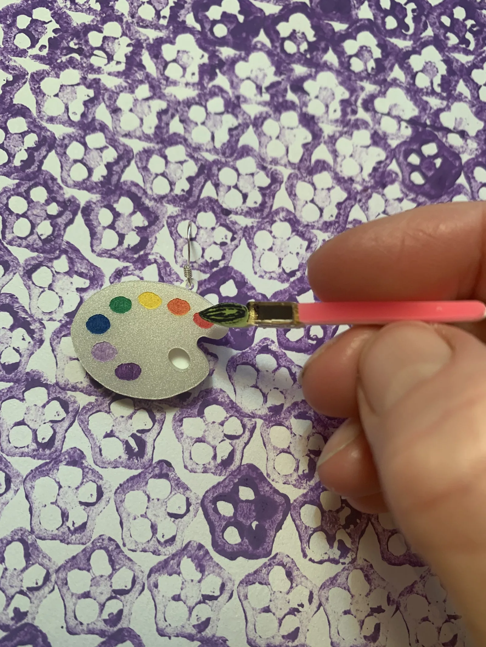 A hand painting colorful dots on a laser-cut artist-palette earring