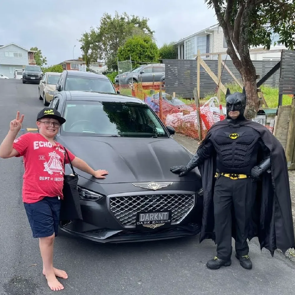 Kit Walker dressed as Batman beside his customized car with a young fan