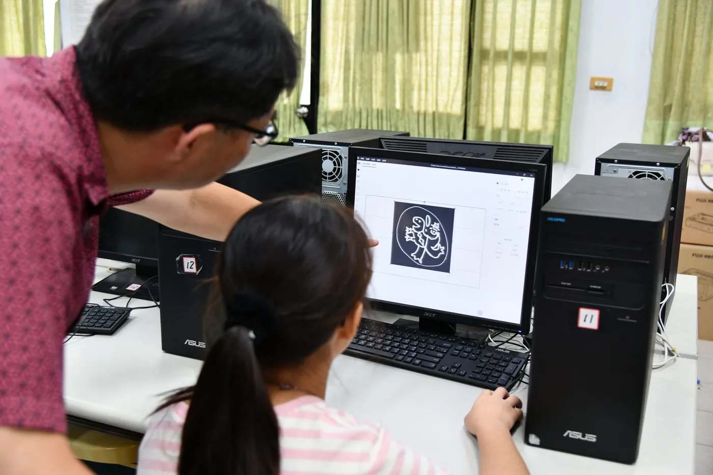 A teacher guiding students as they prepare artwork on a classroom computer