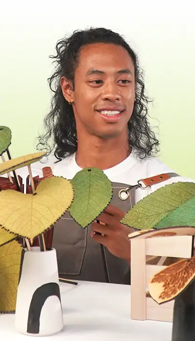 A maker holding a laser-cut botanical artwork beside a vase of paper leaves